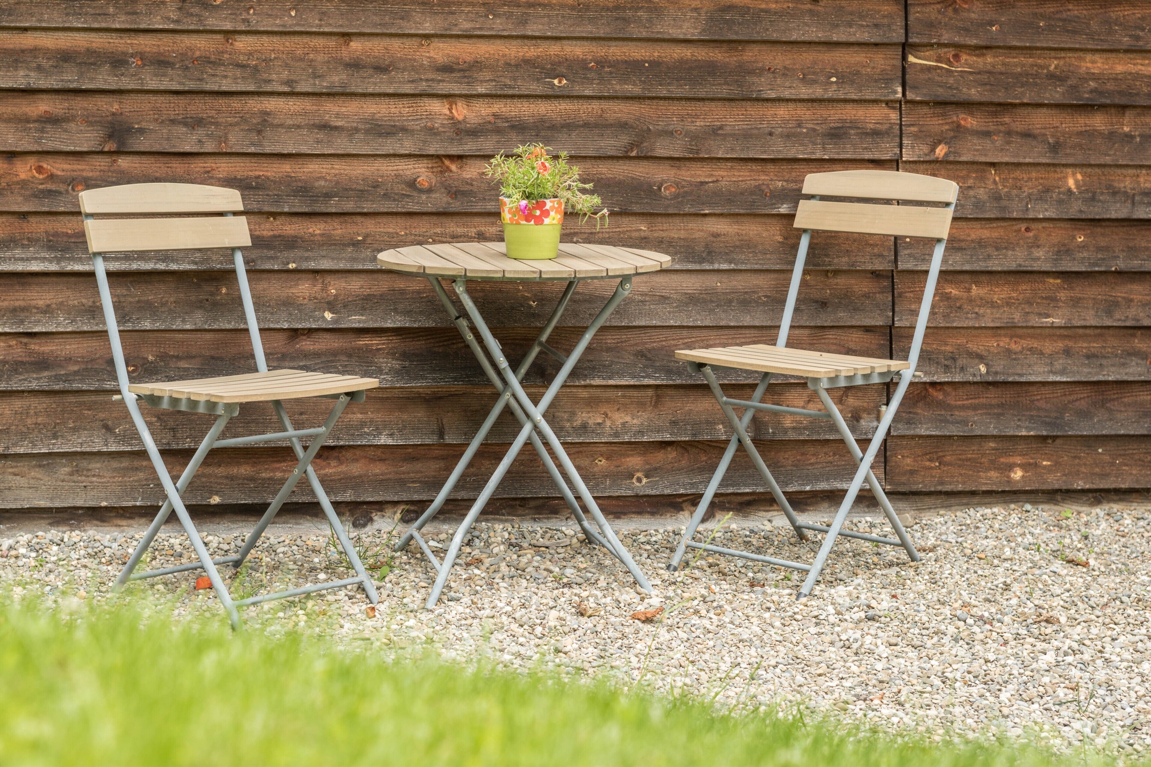 Twee opklapbare stoelen en een kleine ronde tafel met een potplant voor een houten wand.