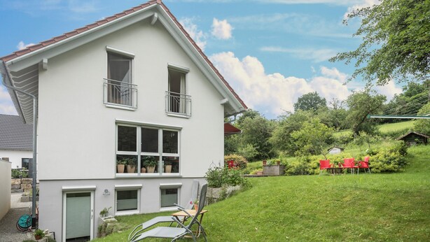 Une maison à deux étages avec un balcon, une pelouse et un petit abri de jardin à l’arrière.