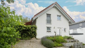 Une maison à deux étages, avec une façade blanche, un toit rouge et une allée gravillonnée.