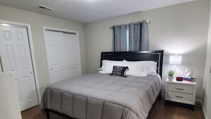 Een slaapkamer met een bed, nachtkastje, lamp en een deur.