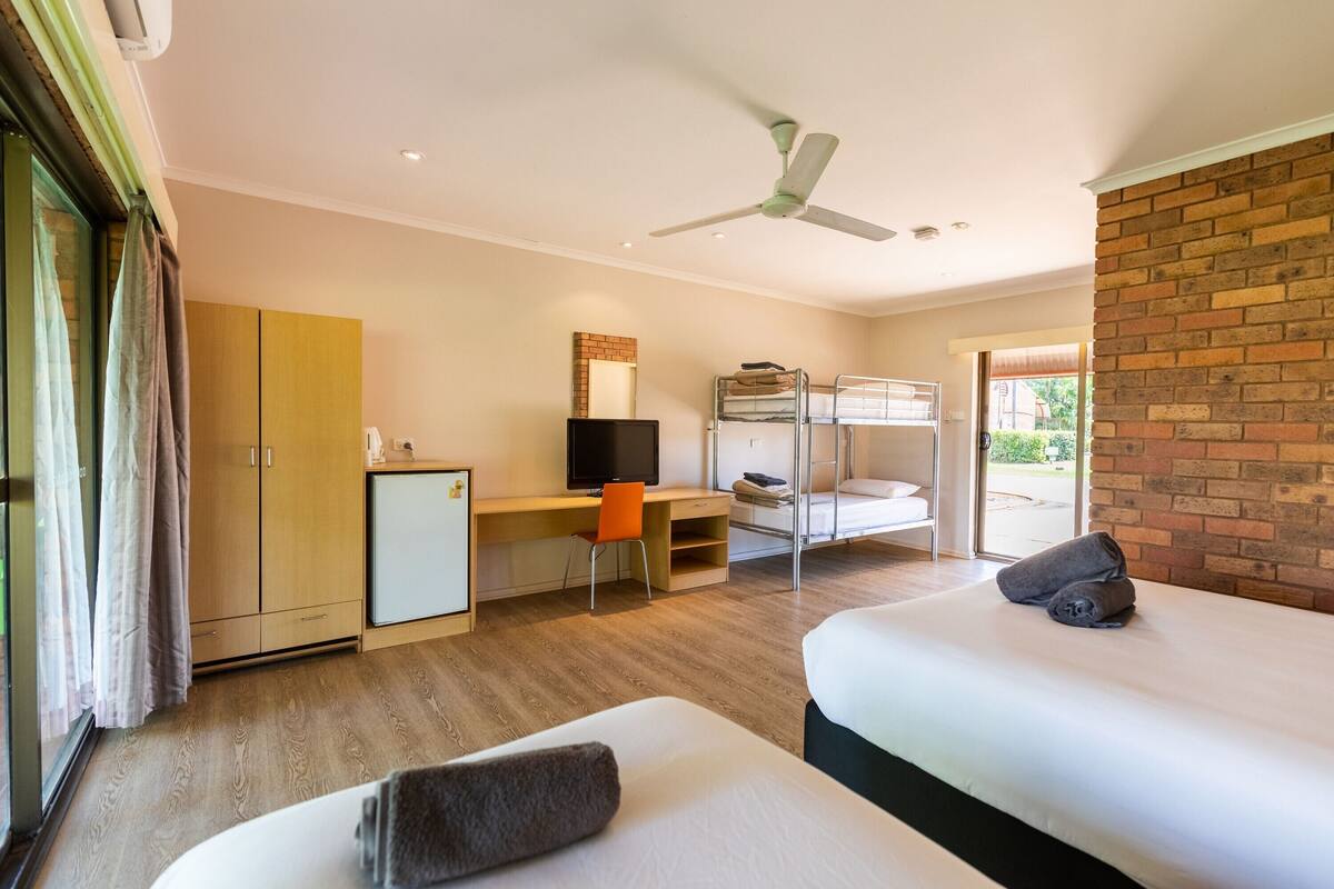 A hotel room with two beds, a desk with a chair, a television, and a wardrobe.