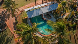An aerial view of a residential area with a swimming pool surrounded by palm trees, a covered outdoor area, and RVs parked nearby. - Contour Hotel Katherine (Katherine East)