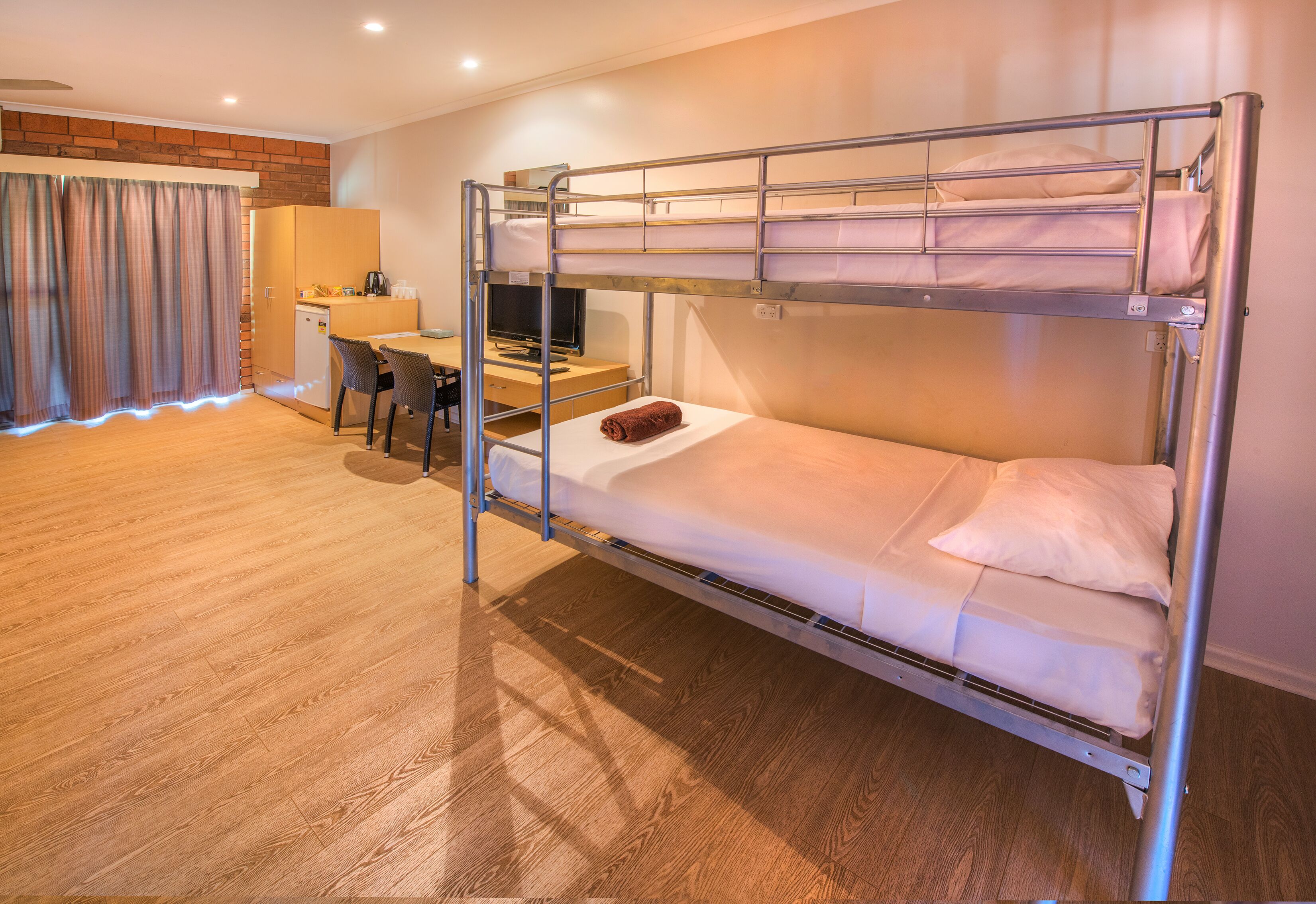 A bunk bed with a desk and chair, a small kitchenette, and a wooden floor.