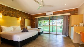 A hotel room with two beds, a desk, a chair, and a large sliding glass door leading to a balcony. - Contour Hotel Katherine (Katherine East)
