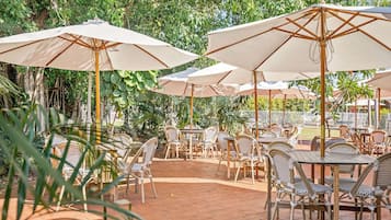 An outdoor patio with tables and chairs, shaded by large umbrellas.