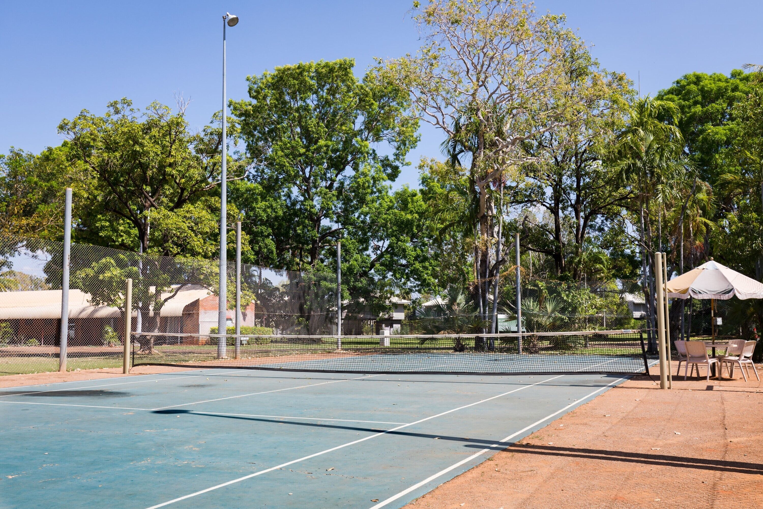 A tennis court with a net, surrounded by trees and a fence.