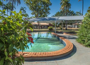 A swimming pool with a brick edge, surrounded by greenery and a covered area with a roof. - Contour Hotel Katherine (Katherine East)