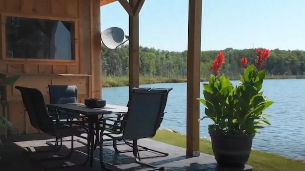 A wooden cabin with a dining area overlooking a lake, a satellite dish, and potted plants. - Top Rated Waterfront Cottage + Sauna | Beach | Private Dock (Georgian Bluffs)
