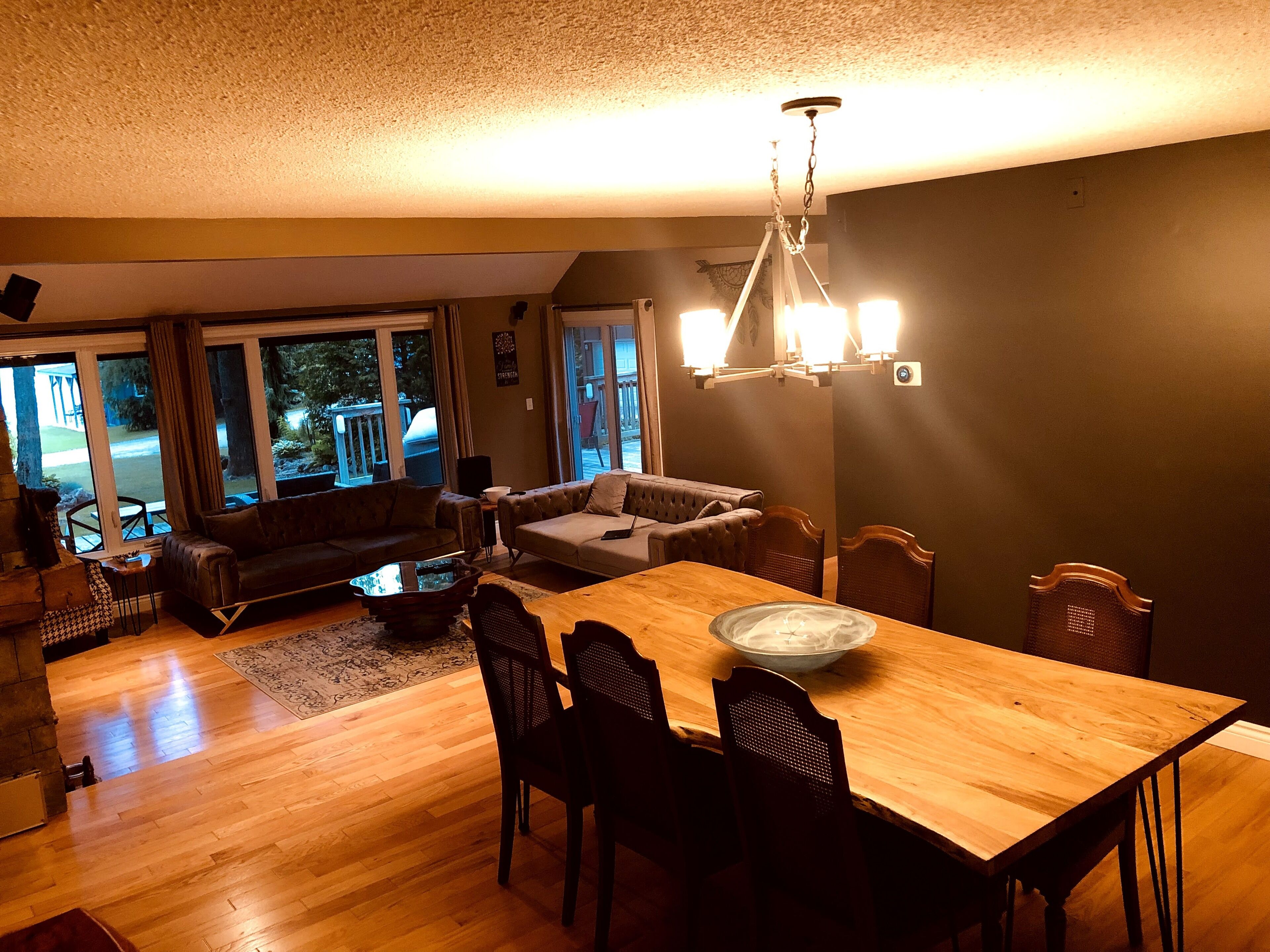 A cozy living room with a wooden dining table, dark sofas, and a chandelier.