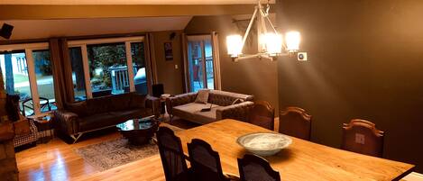A cozy living room with a wooden dining table, dark sofas, and a chandelier.