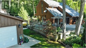 A two-story wooden cabin with a fenced yard, satellite dish, and a garage. - Top Rated Waterfront Cottage + Sauna | Beach | Private Dock (Georgian Bluffs)