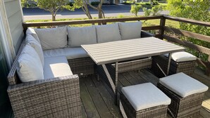 Una terraza de madera con un sofá de mimbre, dos otomanas y una pequeña mesa.