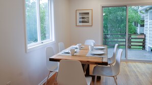 Comedor con mesa de madera dispuesta para cuatro personas, sillas blancas y un ventanal amplio.