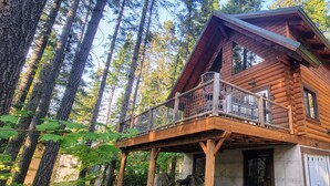 A log cabin with a balcony, surrounded by tall trees.