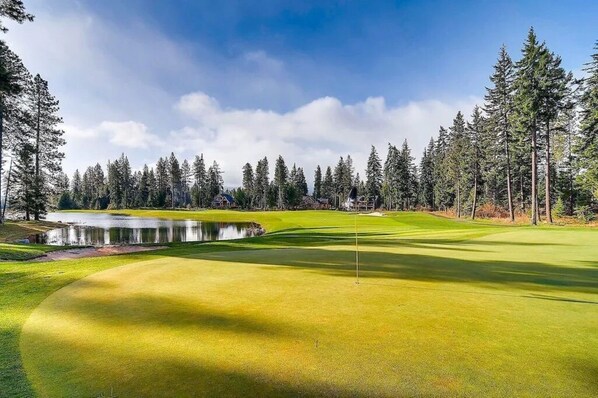 Un campo de golf con un estanque, rodeado de árboles altos y un cielo despejado.