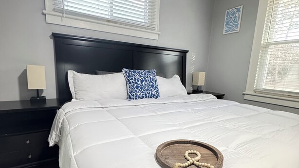 A neatly made bed with a white comforter and a decorative wooden tray with a string of beads.