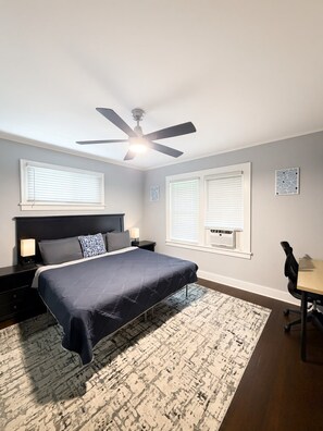 Une chambre à coucher comprenant un lit, des tables de chevet, un bureau et un ventilateur de plafond.