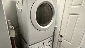 A laundry room with stacked washer and dryer units, a door, and a yellow detergent bottle on the floor.