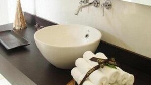 Un baño con un lavamanos blanco, un espejo y una bandeja de madera con toallas enrolladas.