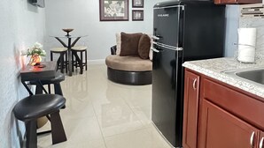 A compact kitchen with a refrigerator, a dining area with a table and chairs, a sofa, and a small rug with fruit design. - Bahía Heaven (Tampa)