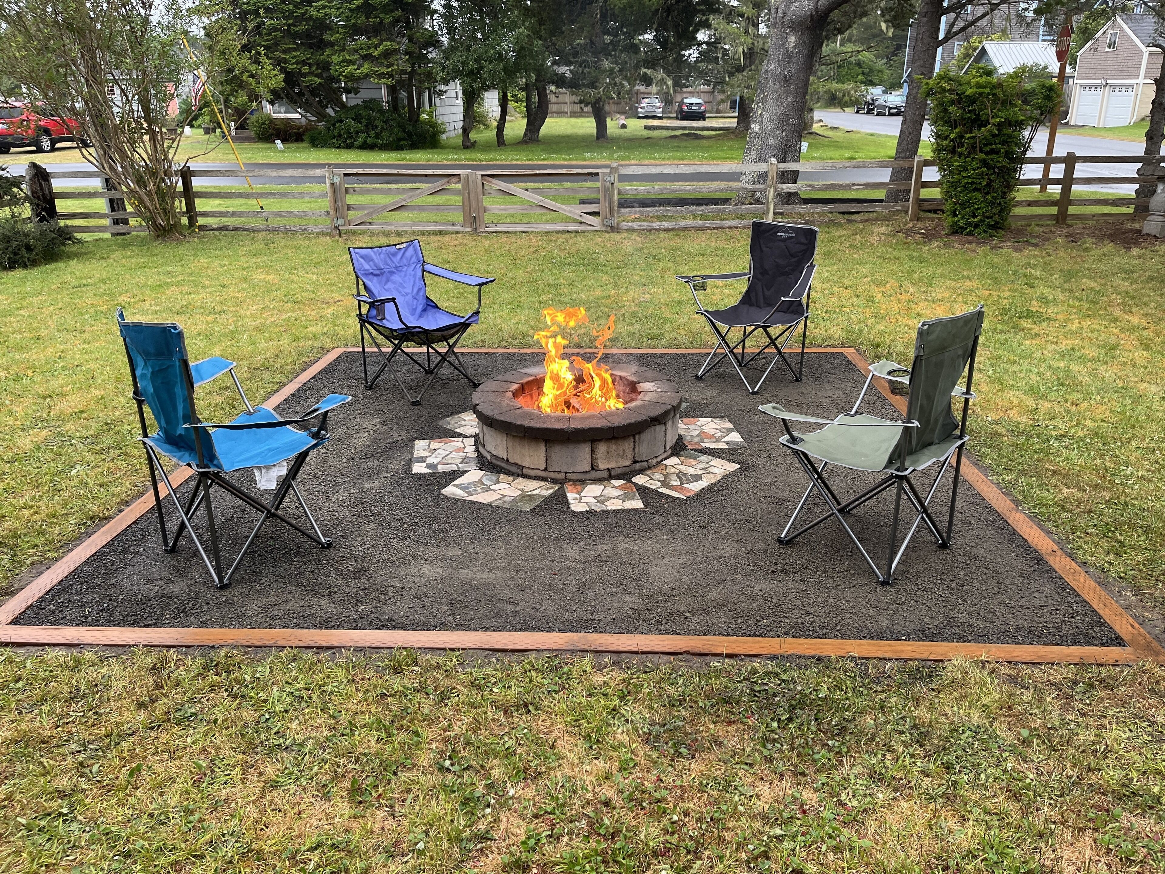 A fire pit with four folding chairs arranged around it on a patio area.
