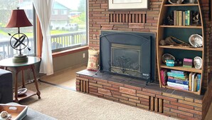 A living room with a brick fireplace, a bookshelf, and a window with curtains. - Charming Private Home - Walk to DT and the Beach! (Long Beach)