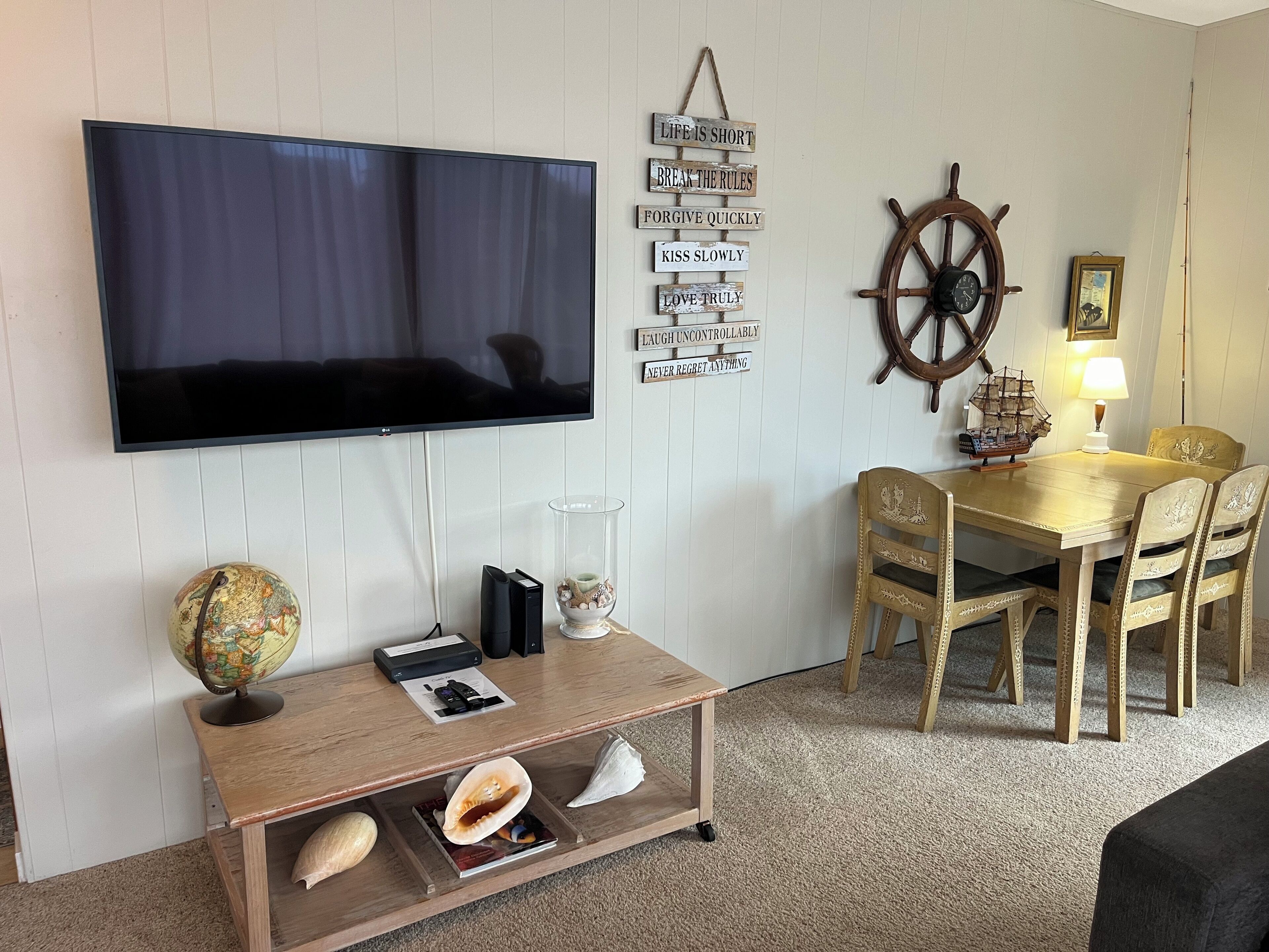 Een woonkamer met een flatscreen televisie, houten meubels, een wereldbol, een scheepsschroef en inspirerende borden aan de muur.