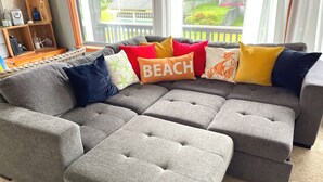 A grey sectional sofa with multiple cushions, including a pillow with the word "BEACH" on it. - Charming Private Home - Walk to DT and the Beach! (Long Beach)