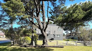 A residential area with a large tree in the foreground, a wooden fence, and houses in the background. - Charming Private Home - Walk to DT and the Beach! (Long Beach)