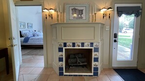 Un pasillo con una chimenea, una puerta con un ventanal y una cama en la habitación contigua.