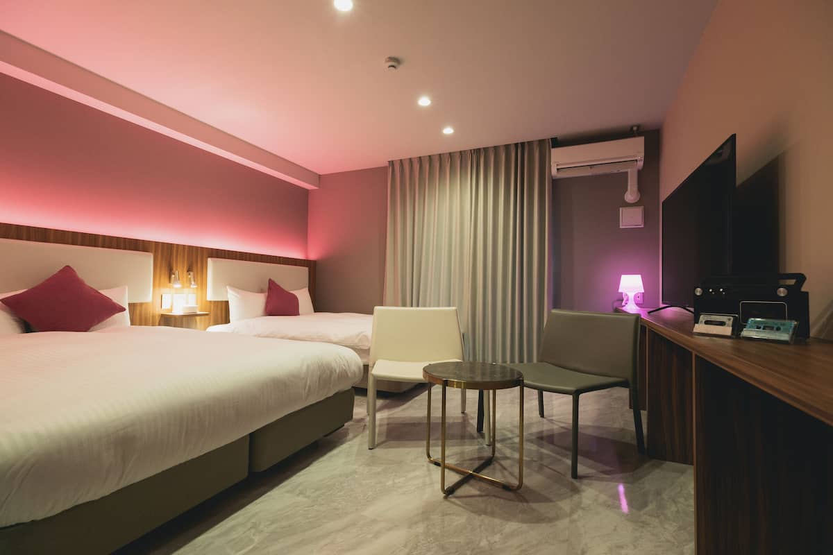 Ein Hotelzimmer mit einem Bett, zwei Sesseln, einem kleinen Tisch, einem Schreibtisch mit Radio und einem Fernseher.