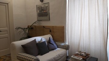 Habitación con sofá blanco, cabecera de madera, planta en maceta y un cartel con etiqueta de precio.