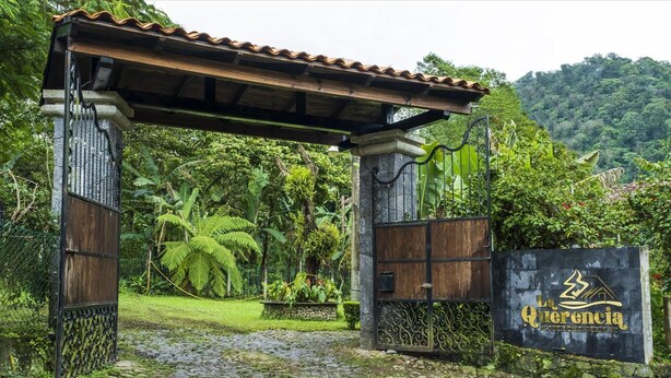 A wooden gate with a metal gate, a stone pillar, and a sign with the text "La Querencia". - Posada La Querencia (Xico)