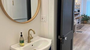 A bathroom with a white sink, a round mirror, and dark blue cabinets.