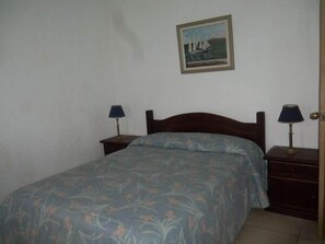 A single bed with a floral bedspread, two bedside tables with lamps, and a framed painting of sailboats on the wall. - Hotel La Pedrera (La Pedrera)