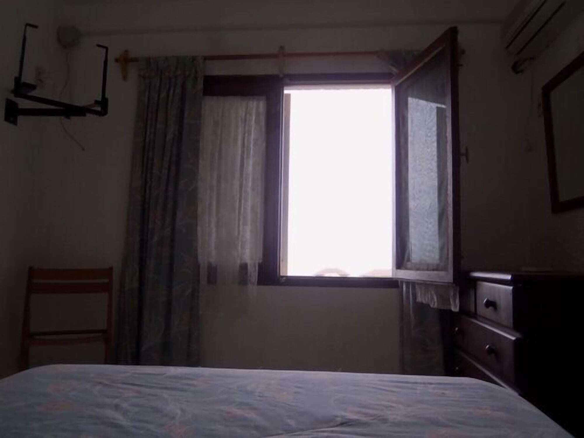 Une chambre à coucher avec un lit, une chaise, une commode et une fenêtre avec des rideaux.