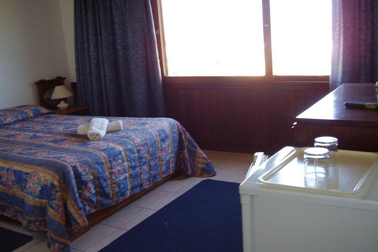 Een hotelkamer met een bed, bureau, lamp en raam met gordijnen.