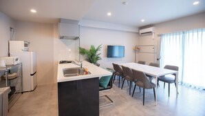 A modern kitchen with a central island, a dining area with a table and chairs, a flat-screen TV mounted on the wall, and a large window with curtains. - HOTEL SO SUMIYOSHI (Fukuoka)