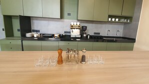 Una cocina con armarios verdes, una cafetera y una mesa de madera con vasos y un molinillo de pimienta.