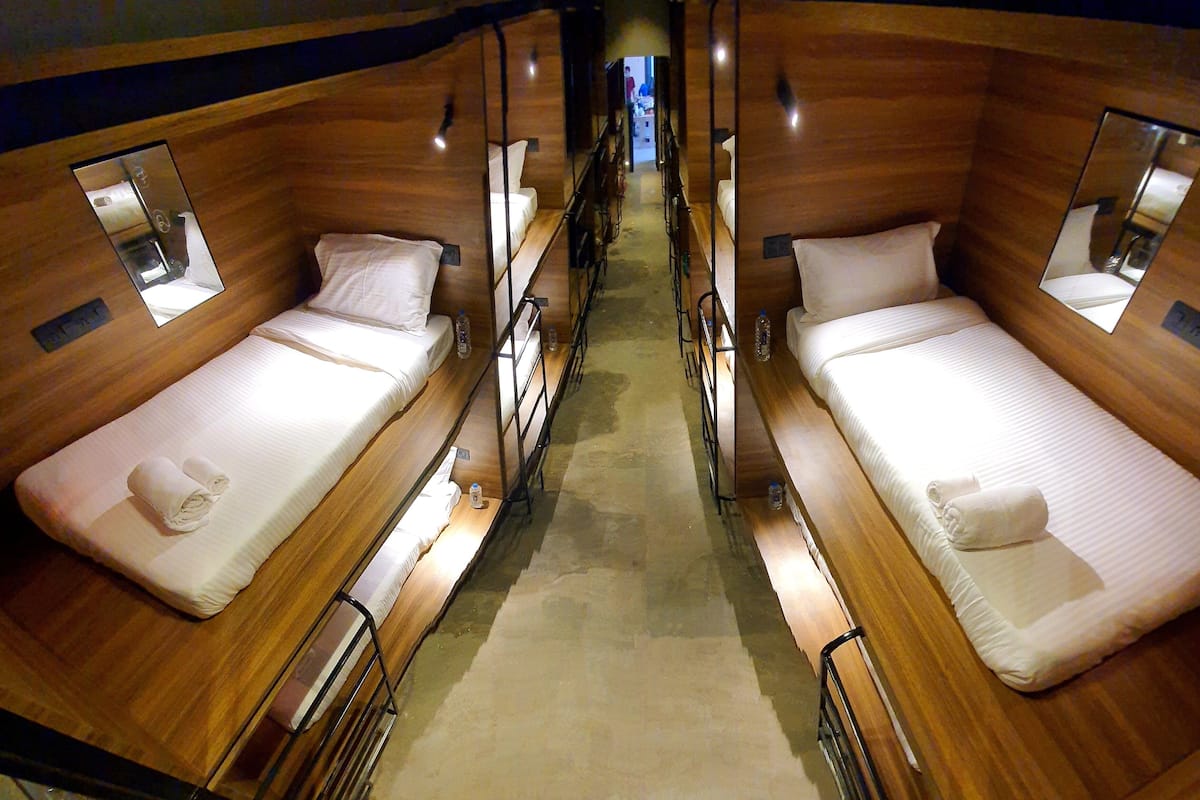 A narrow, wooden-paneled room with two single beds, each with a small bedside table and a mirror.