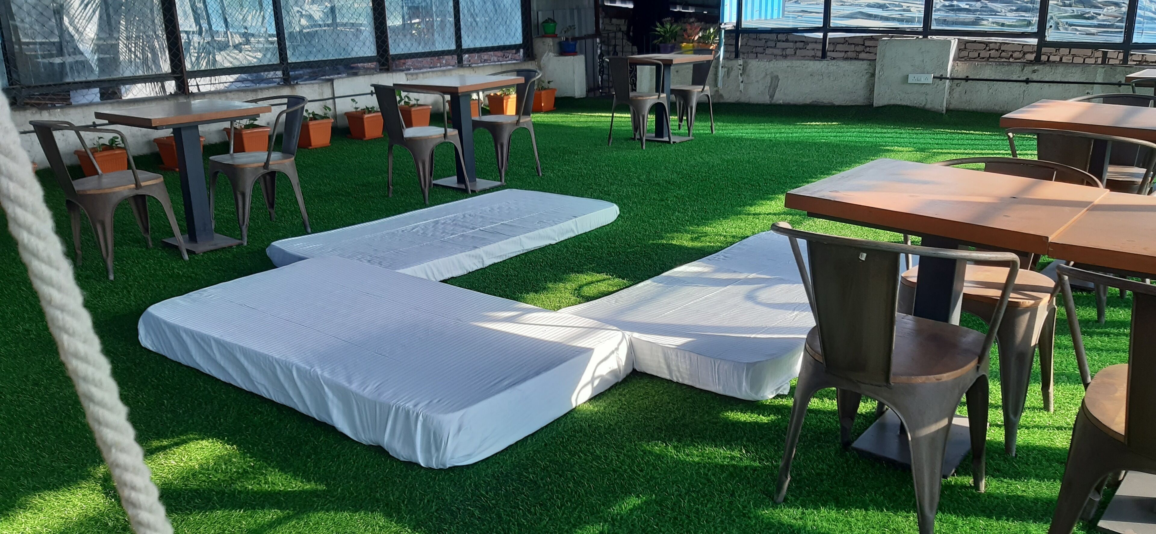 An outdoor seating area with tables and chairs, artificial grass, and a view through a fence.