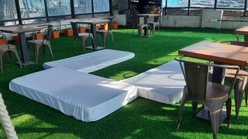 An outdoor seating area with tables and chairs, artificial grass, and a view through a fence.