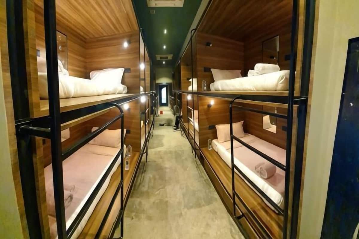 A narrow corridor with bunk beds on either side, wooden walls, and a concrete floor.