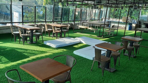 Un área de estar al aire libre con mesas y sillas, rodeada de amplios ventanales y vegetación.