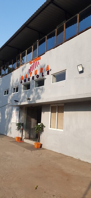 A building with a sign reading "CO-LOADING MAYURA AUREOLE" and a signboard listing services like "BED & BREAKFAST," "BIRDS," "CONDOMINIUM," "HOTEL," "SOHO," and "BUSINESS TRAVEL." - Mayura Aureole Co-living - Hostel (Mumbai)