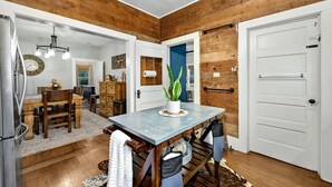 Una cocina rústica con paredes de madera, un comedor con una mesa y sillas de madera, un refrigerador y una planta en maceta sobre la encimera.