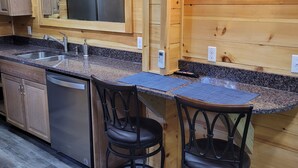 A modern kitchen with wooden paneling, granite countertops, stainless steel appliances, and two bar stools. - Adorable garden level condo with courtyard and firepit (Rutherfordton)