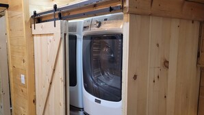 A laundry room with two stacked washing machines, wooden walls, and a metal rack on top. - Adorable garden level condo with courtyard and firepit (Rutherfordton)