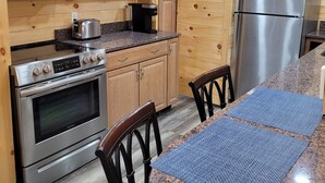 A modern kitchen with wooden paneling, stainless steel appliances, granite countertops, and a dining area with a granite table and chairs. - Adorable garden level condo with courtyard and firepit (Rutherfordton)