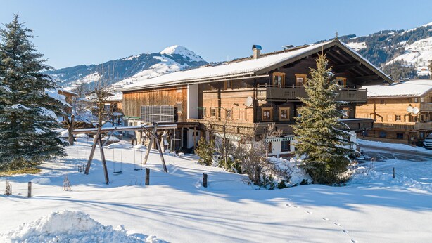 Een houten chalet met een balkon, omringd door besneeuwde grond en bergen op de achtergrond.